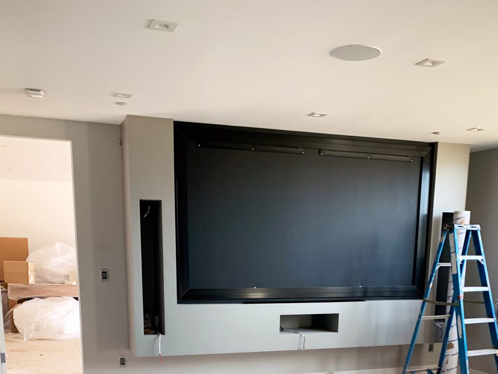 Home theater screen projector installed on a wall with a ladder next to it.